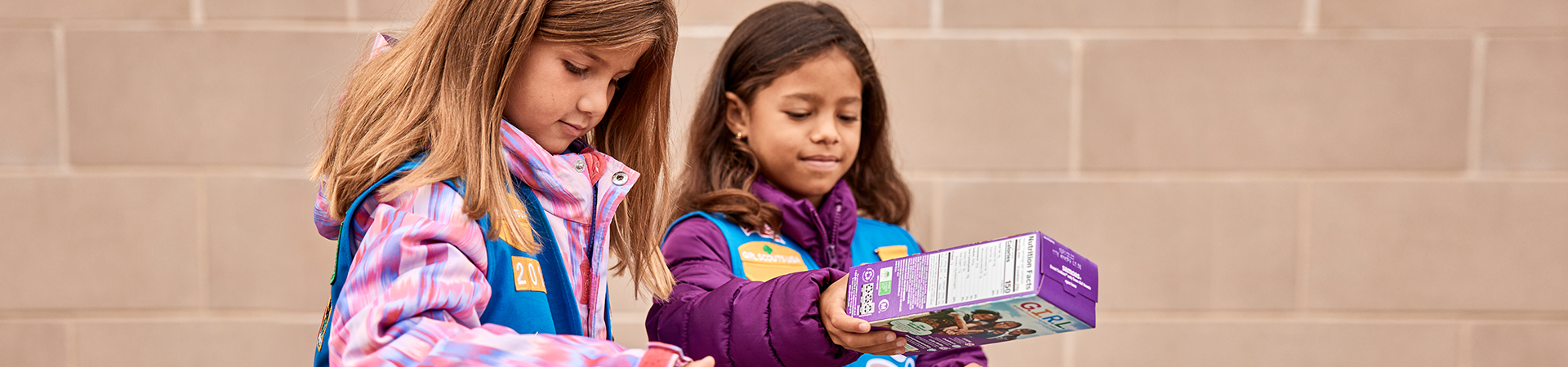  girl scouts selling cookies with one girl in front of booth holding sign that says "girl scout cookie proceeds stay local" 