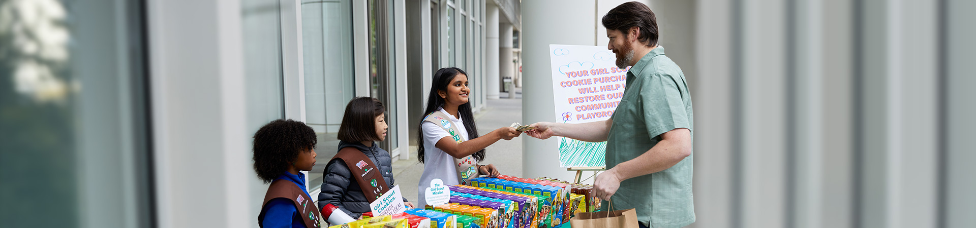  hands of young girl scout holding cookie box and handing it to a customer at an outdoor cookie booth 