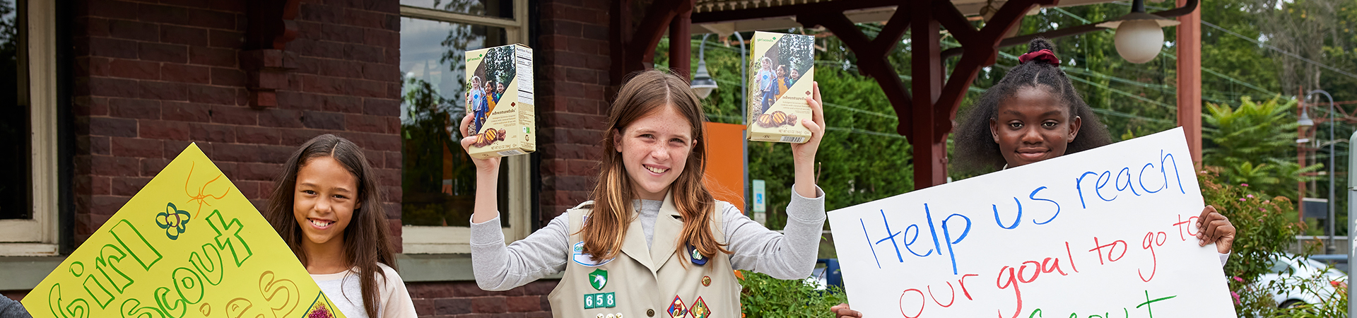  hands of young girl scout holding cookie box and handing it to a customer at an outdoor cookie booth 