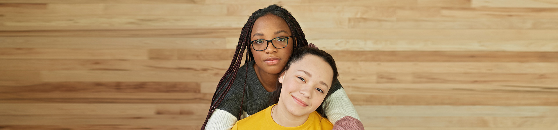  two high school girls hugging while staring at the camera with content facial expressions 